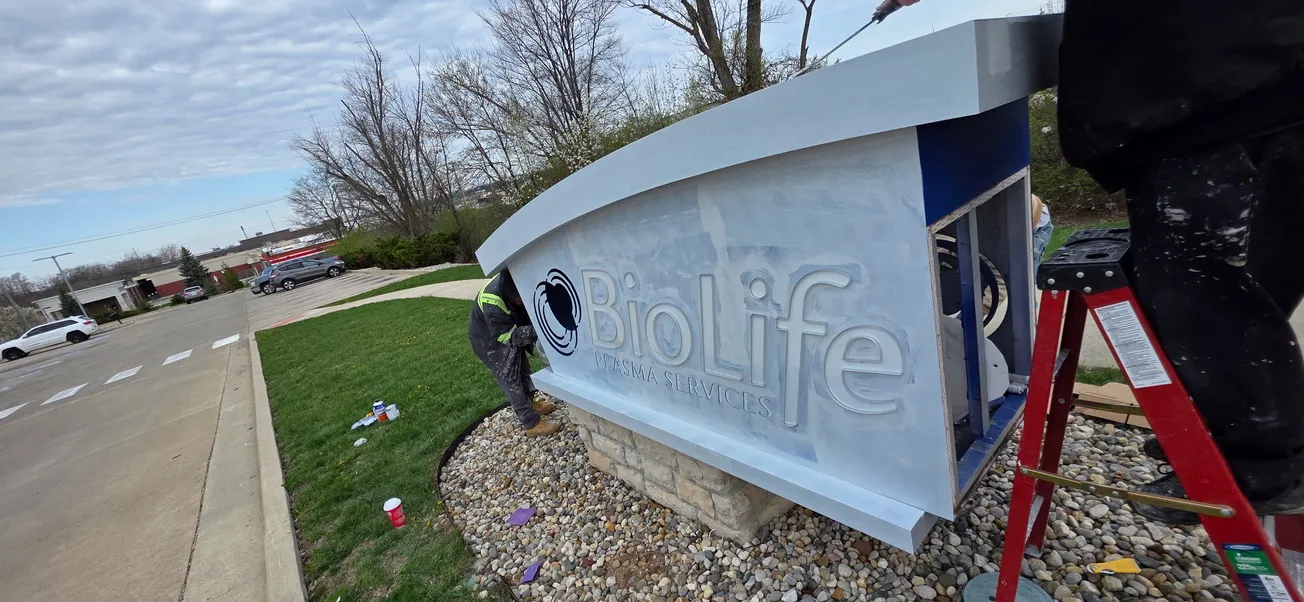 Medical facility monument sign being painted by National Painting Partners crew member on ladder in Fort Wayne, IN